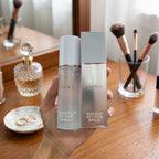 A hand holds a bottle and matching box of RIBORY Makeup Setting Spray in front of a wooden cosmetics display shelf.