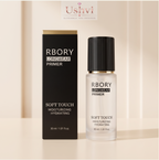 RBORY Longwear Primer Soft Touch moisturizing hydrating primer shown in a clear bottle with a black cap next to its black packaging box with gold accents, set against a warm beige background with a soft vertical gradient.