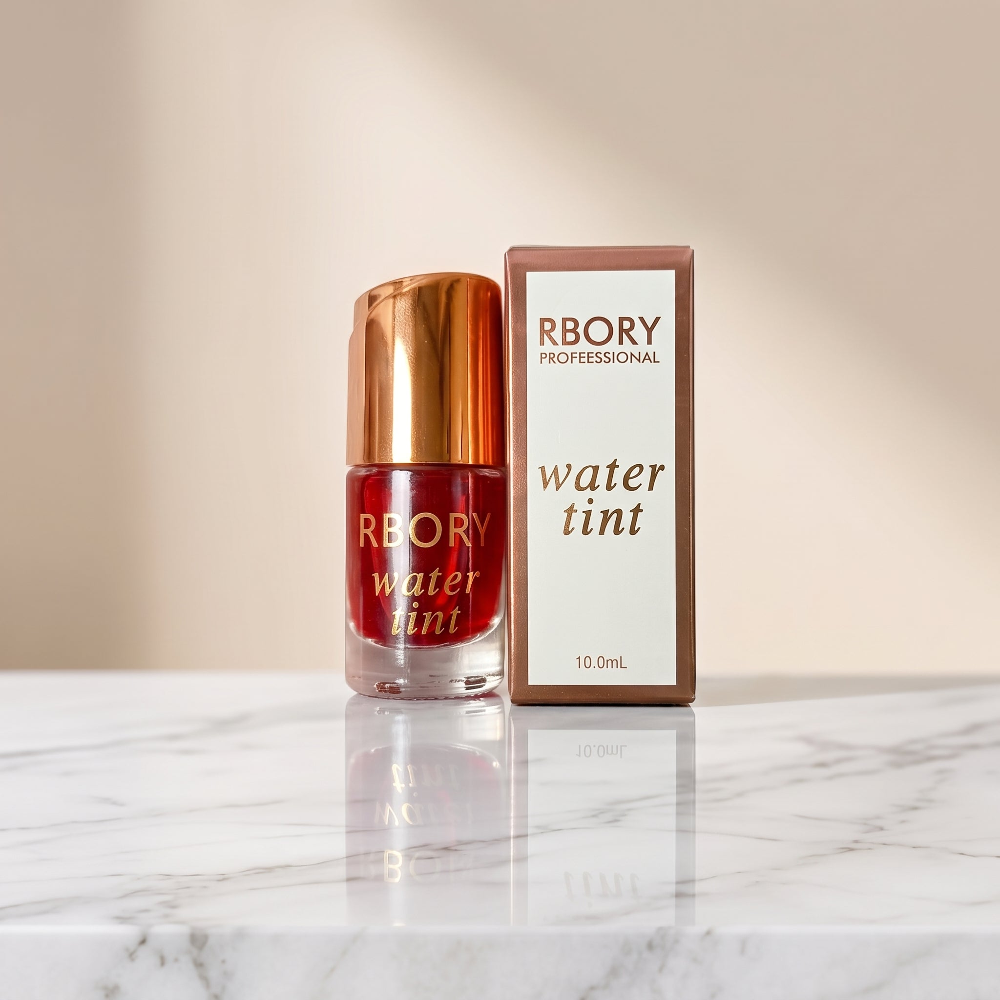 RBORY Professional water tint bottle with a metallic gold cap next to its retail box, displayed on a white surface over artificial green grass against a white backdrop.Ushvi.pk
