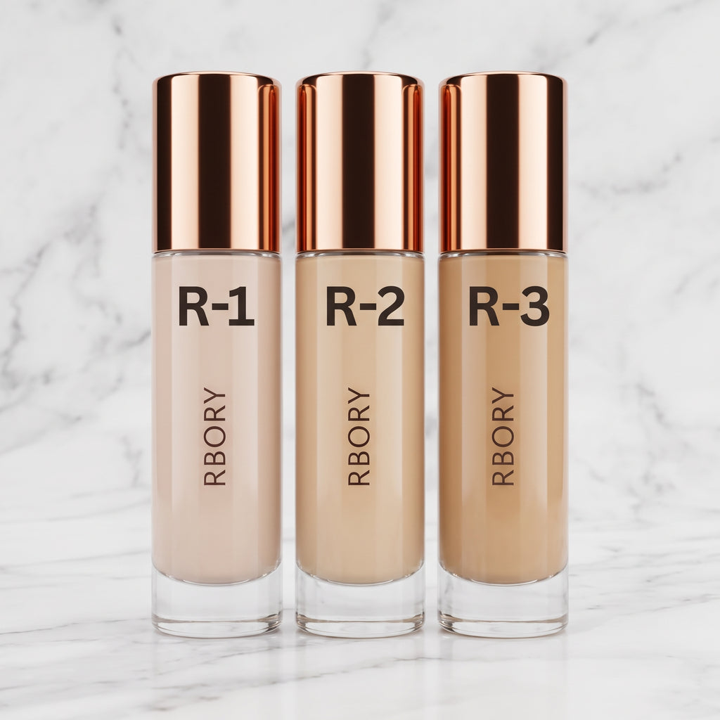 Three bottles of RBORY liquid foundation in shades R-1, R-2, and R-3, arranged side-by-side on a green grass background.
