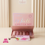 An open pink Miss Royal Matte Lipstick Set box displayed on a beige surface with vertical beige drapery in the background. Several lipsticks in nude pink shades are visible inside the box, and a small pink free gift card is placed in front.