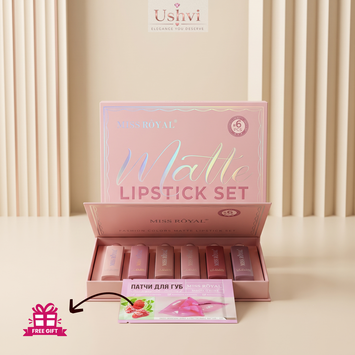 An open pink Miss Royal Matte Lipstick Set box displayed on a beige surface with vertical beige drapery in the background. Several lipsticks in nude pink shades are visible inside the box, and a small pink free gift card is placed in front.