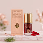 Rose Berry Rose Tinted Lip and Cheek Stain Water-Tint bottle with its pink packaging box, displayed on a white stand with artificial green grass in the background.Ushvi.pk
